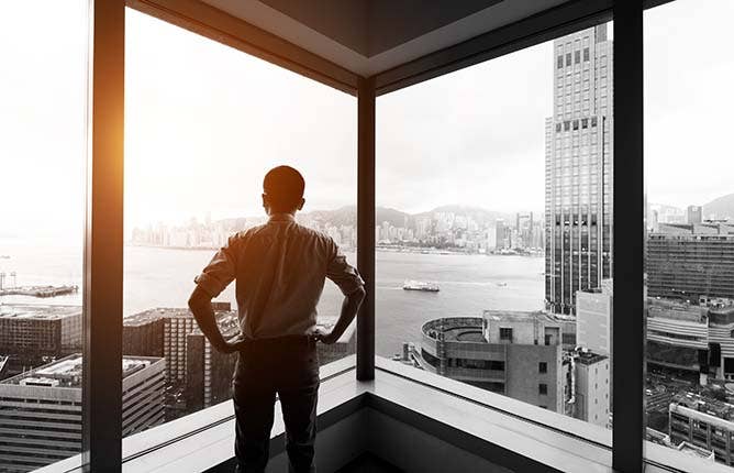 Businessman looking at city through office window.