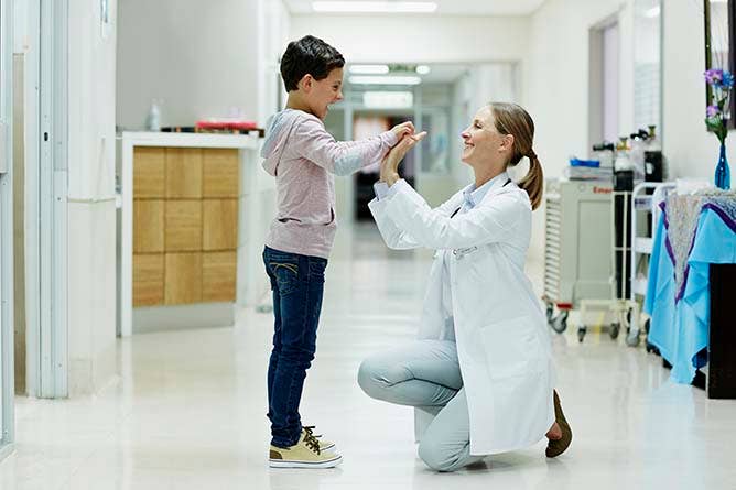 Full length side view of female doctor giving high-five to boy in hospital corridor