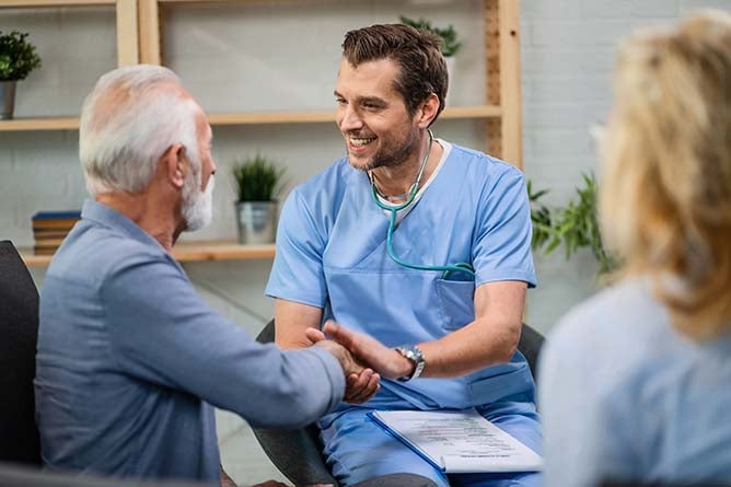 Happy doctor greeting with senior man and shaking hands with him while being in a home visit.