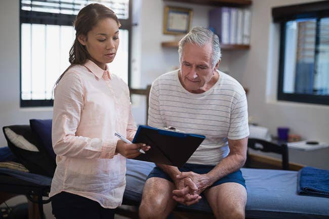 Woman reviewing medical information with older patient sitting in street clothes on table
