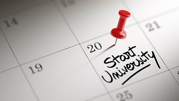 Concept image of a Calendar with a red push pin. Closeup shot of a thumbtack attached. The words Start University written on a white notebook to remind you an important appointment.
