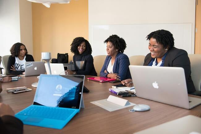 Four black women in an office setting at a conference room table