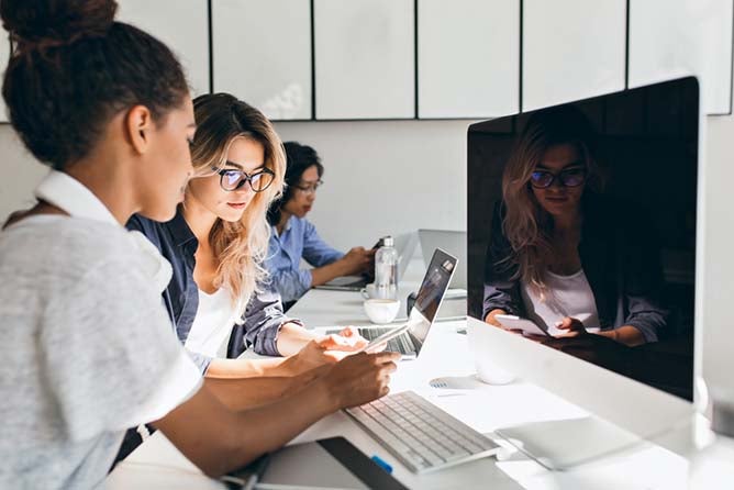 Black female it-specialist sitting beside modern computer with black screen and talking with friends. Indoor portrait of busy young people working in international company.; Shutterstock ID 1013760160; PO: 123